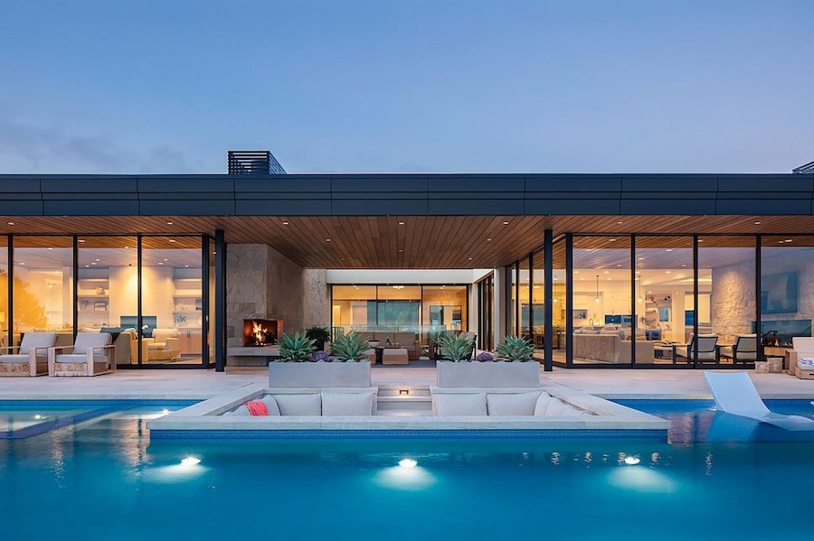A poolside property has floor-to-ceiling windows showcasing softly illuminated indoor spaces. 