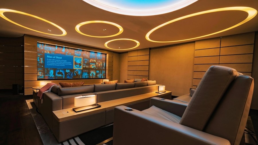 Custom home theater room with circular ceiling lights shining on tiered seating and a large display screen.