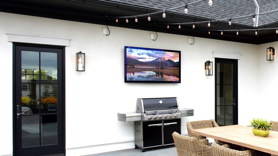 Séura outdoor TV mounted on a wall near a grill and dining area.